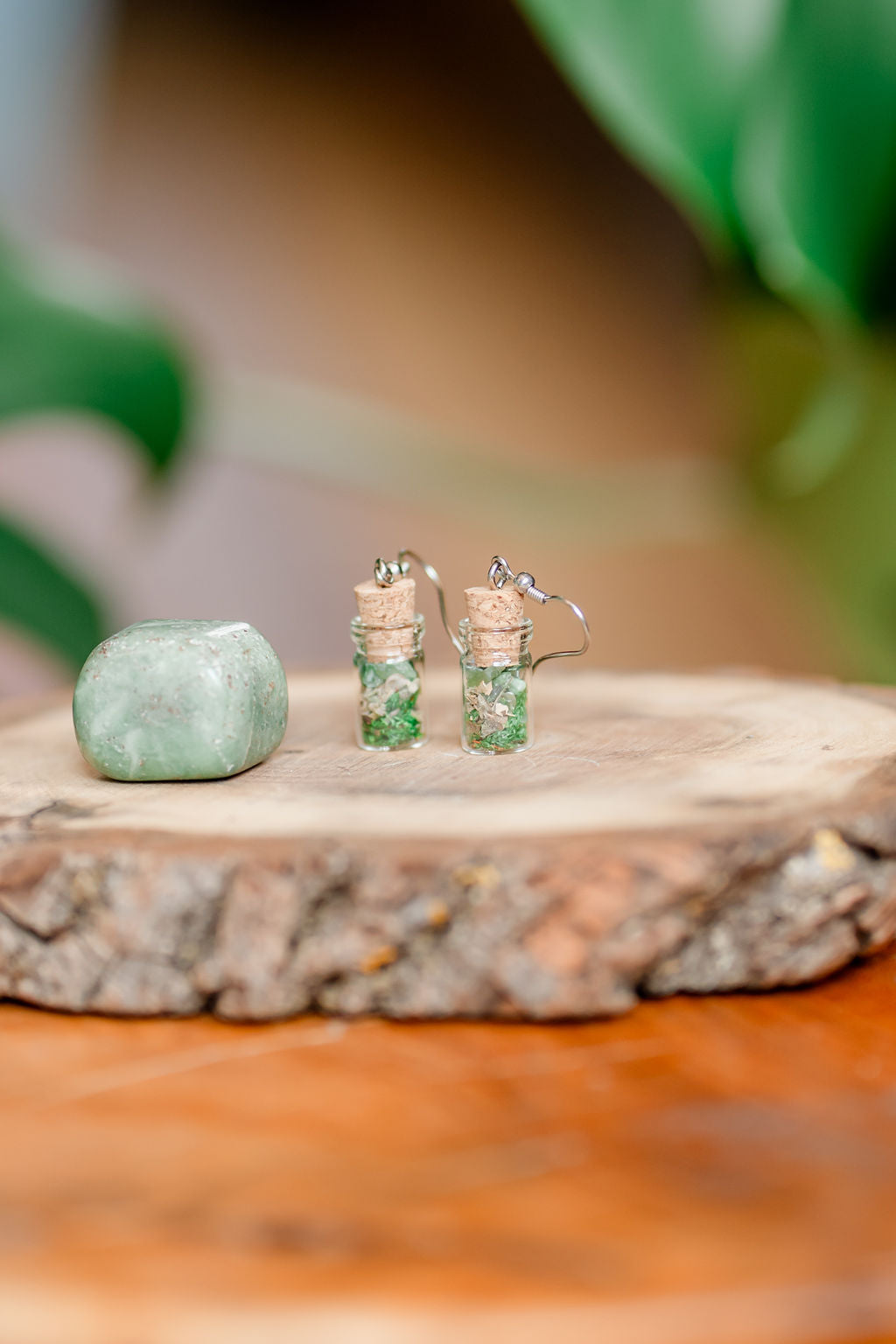 A pair of spell jar earrings with herbs and crystals displayed on a wooden slice.