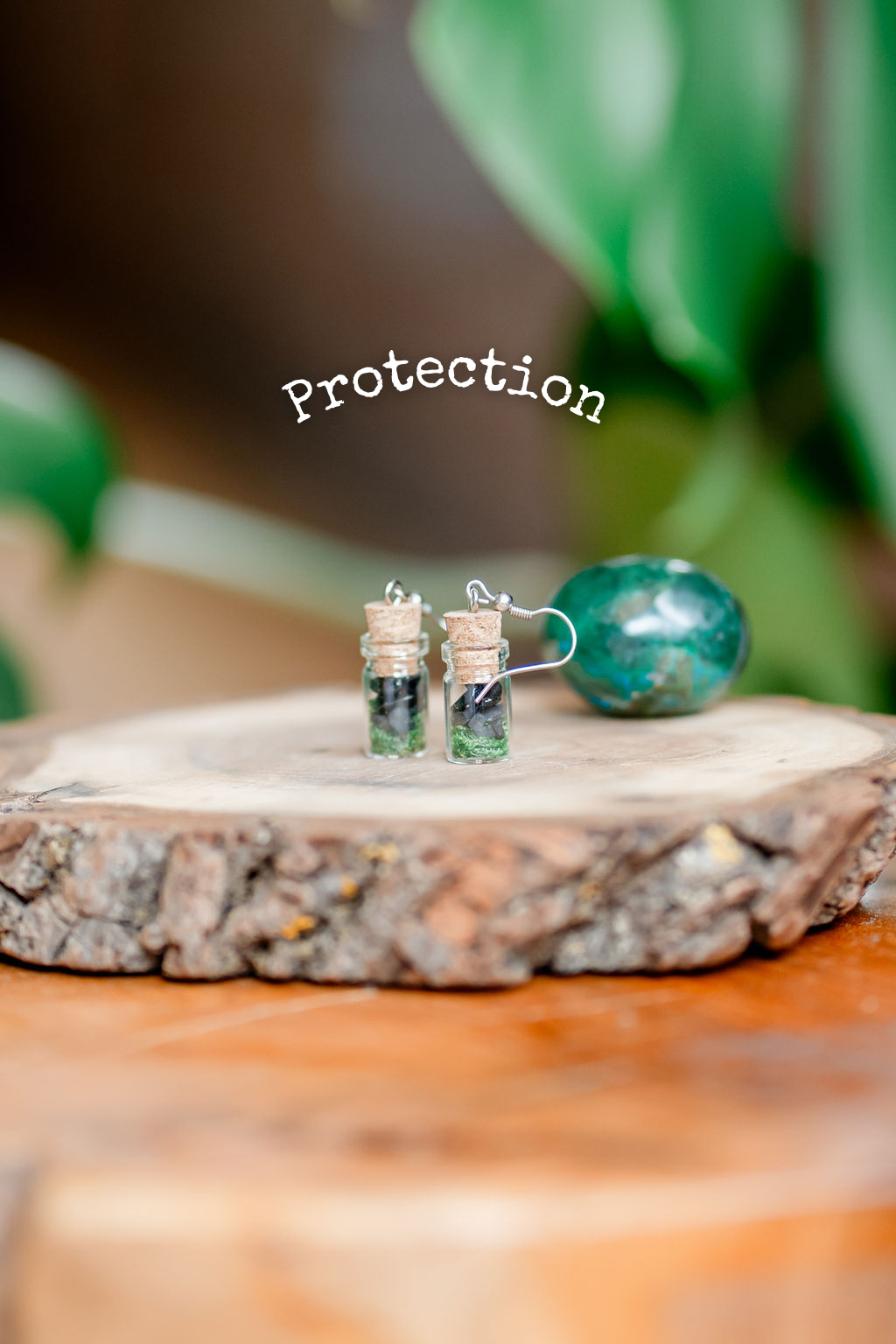 A pair of spell jar earrings with herbs and crystals displayed on a wooden platform, with a protective label above.